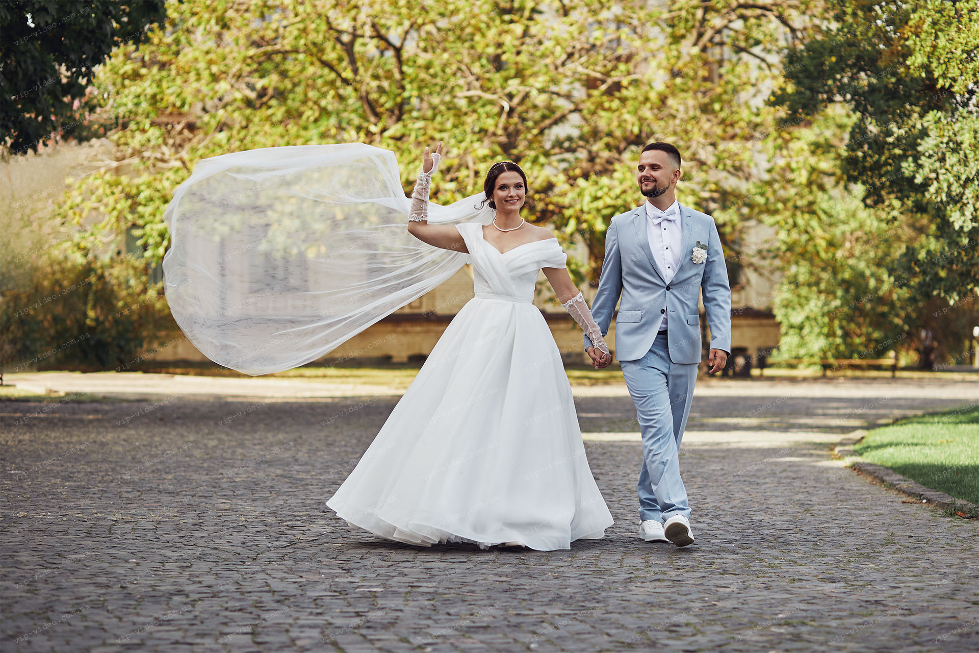 Весільна фотографія на якій зображені молодята у весь зріст і у нареченої розвивається фата