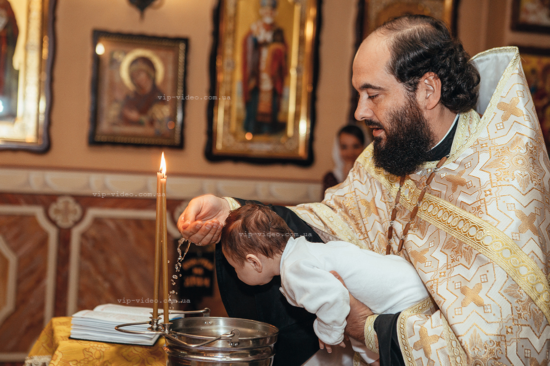 Фотографія на якій священник обливає святою водою малюка під час обряду Хрещення