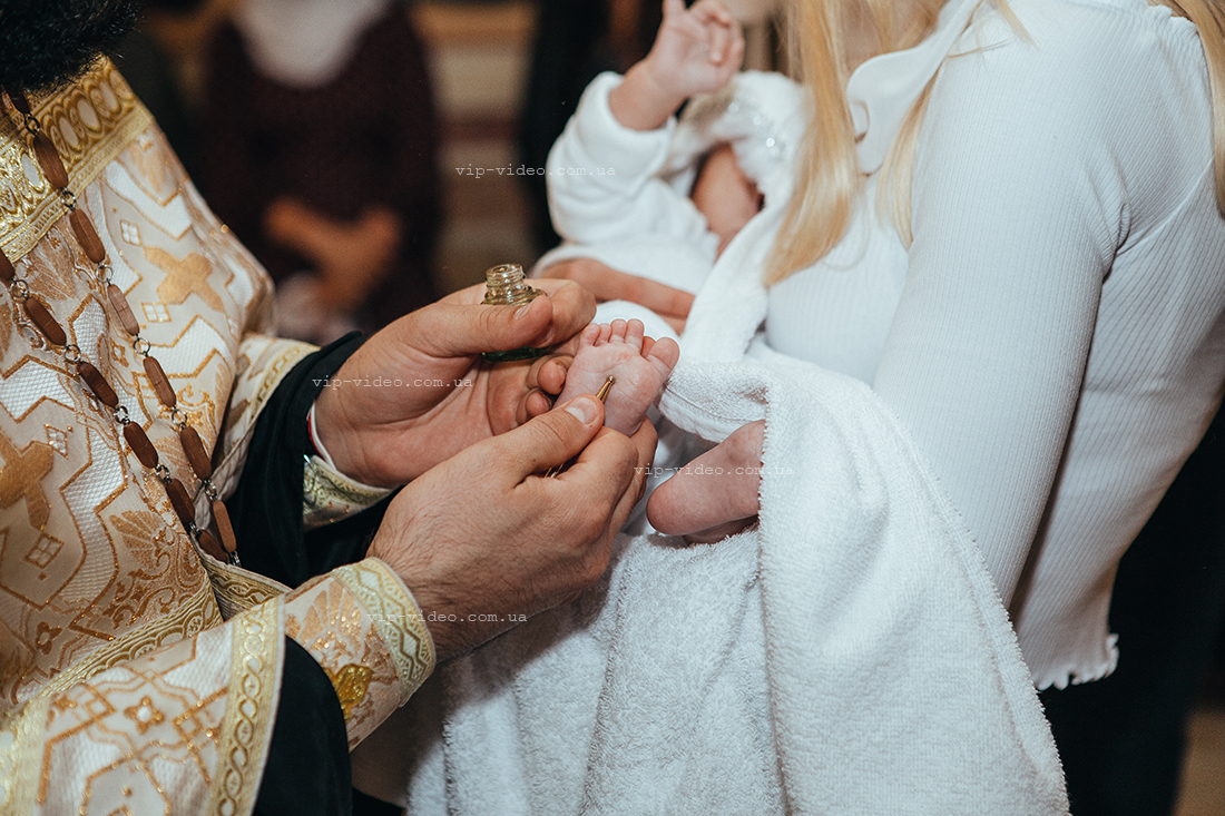 Фотографія на якій церковний священний виконує одну з процедур під час Хрещення дитини, а саме обряд помазання ніжок