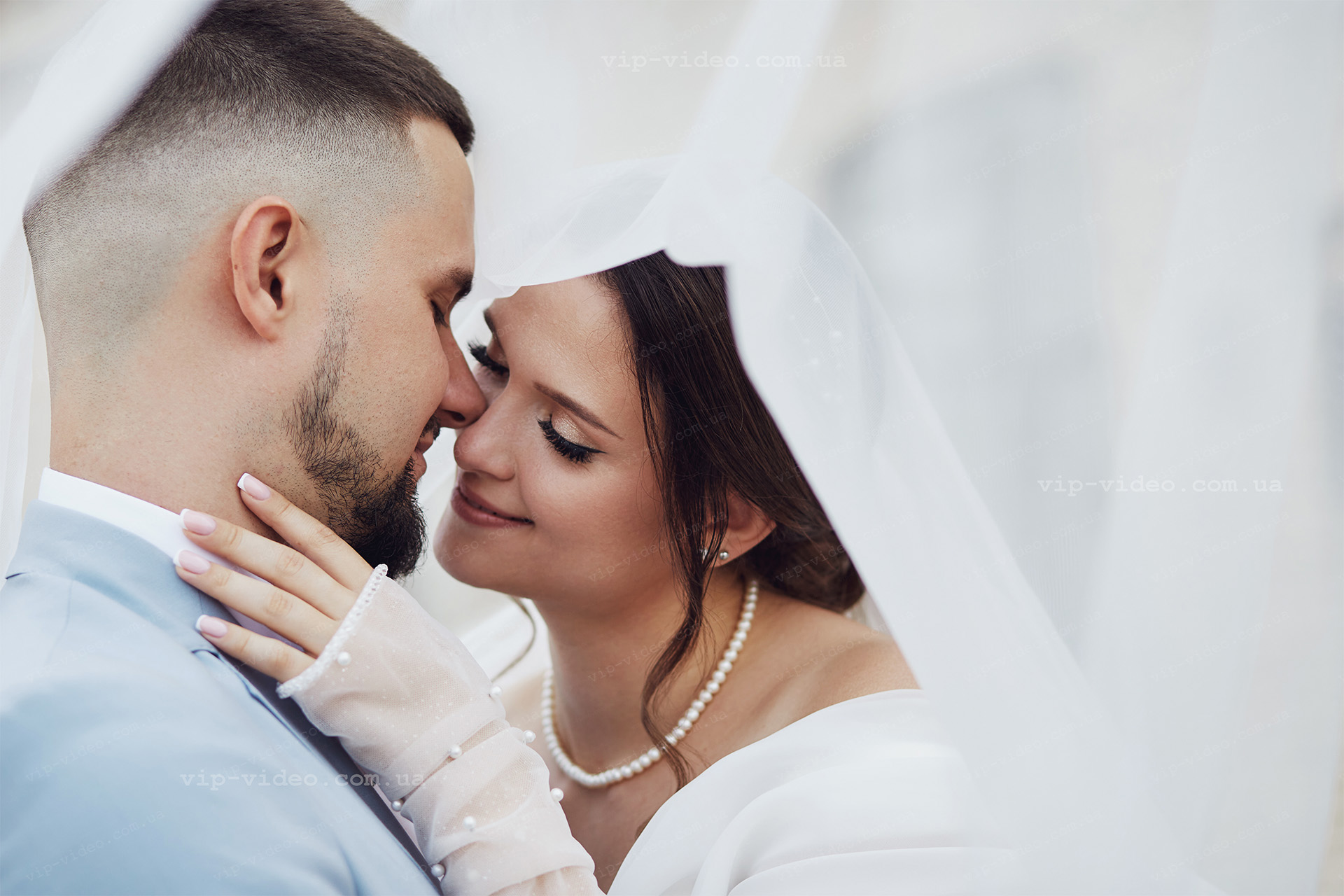 Весільна фотографія де зображені молодята крупним планом під час ніжних дотиків друг до друга на фоні фати нареченої